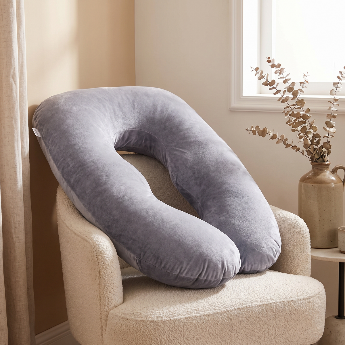 Pregnancy pillow resting on a cream armchair in a calm bedroom