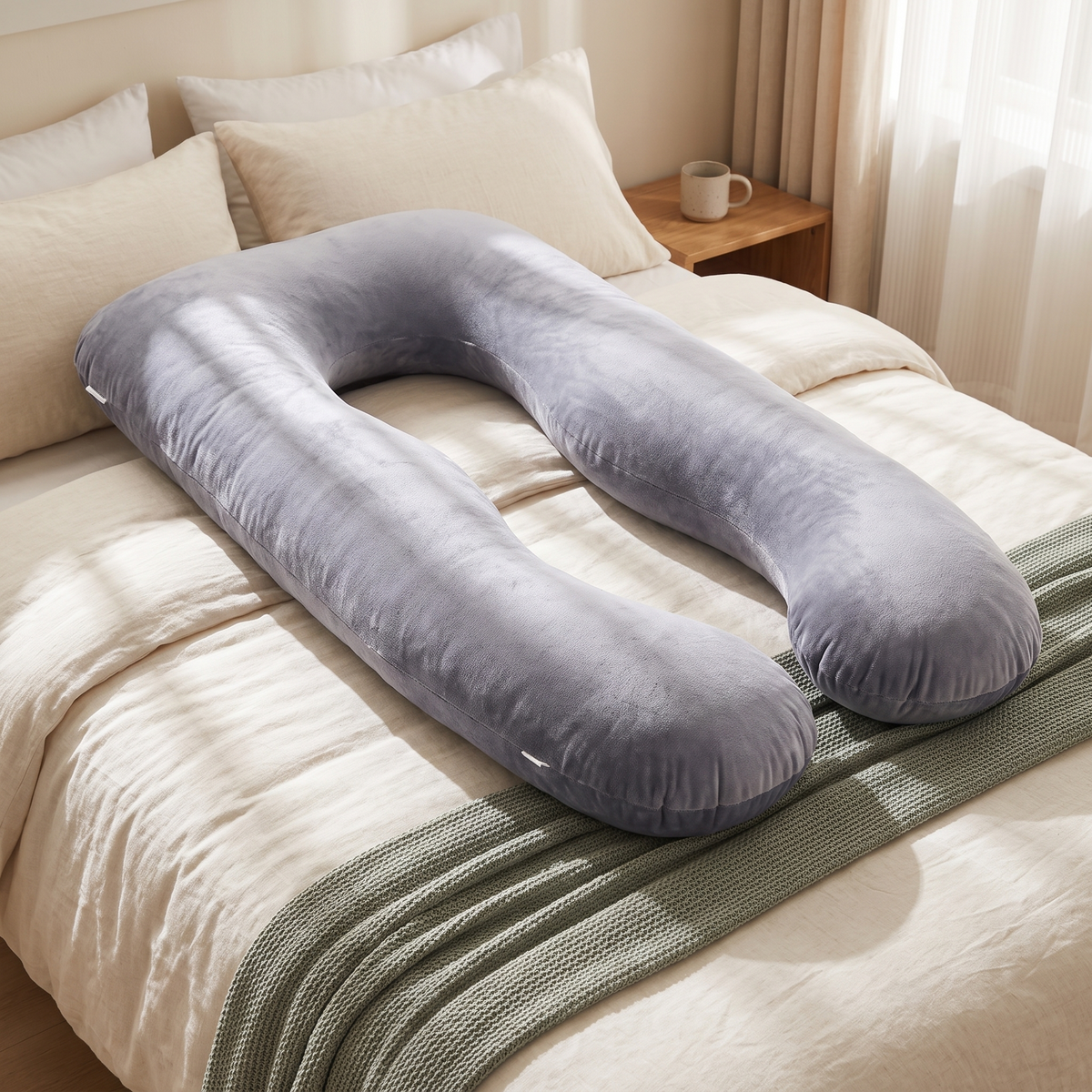 Full-body pregnancy pillow arranged on a bed with cream linen bedding
