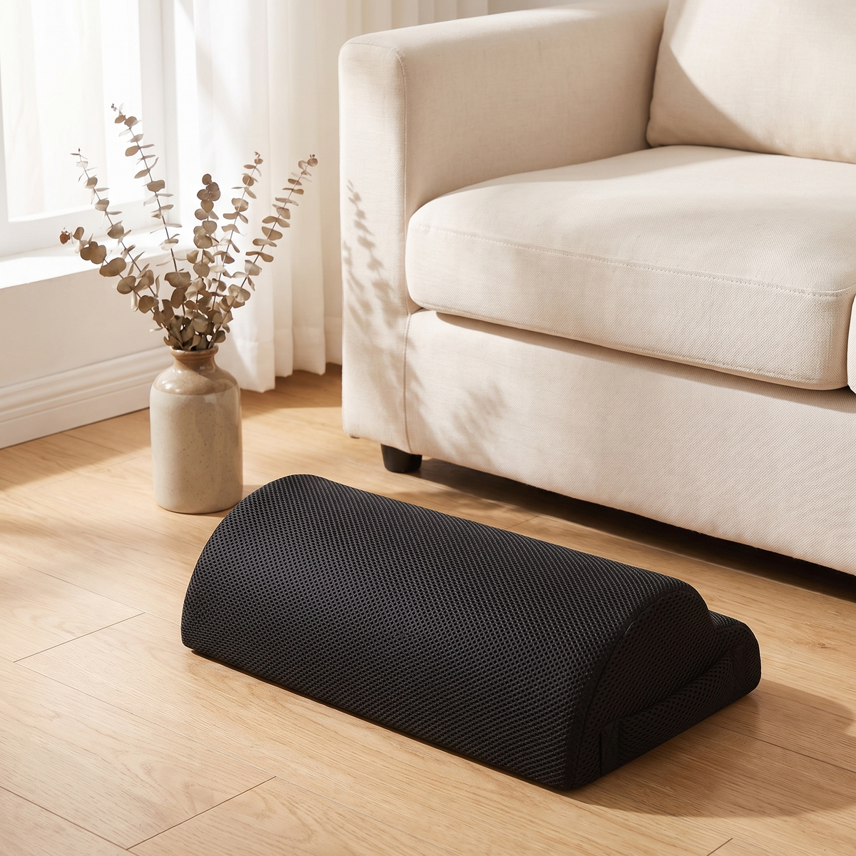 Memory foam footrest placed on a light oak floor beside a cream sofa