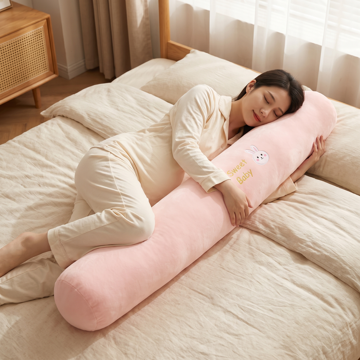 Pregnant woman lying on her side hugging the long bolster pillow with her knees resting on it